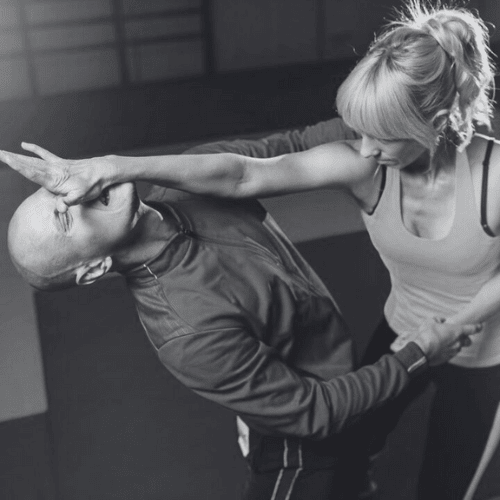 A woman demonstrates a self-defense move, pressing her hand against a man's face during a training session.